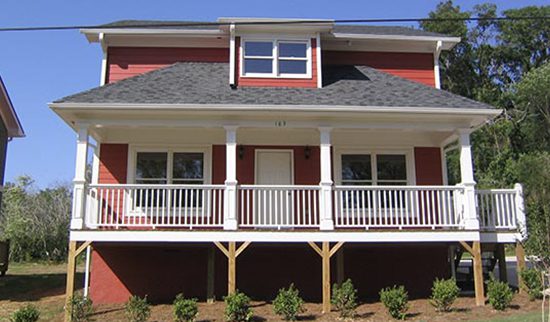 Front view of a red two-story cottage with white trim and porch from the Mandyville community