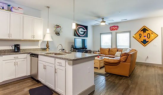 Kitchen and living room with brown couches, white cabinets and silver appliances.