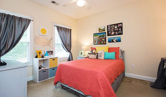 Organized bedroom with bed neatly made with a coral colored comforter.