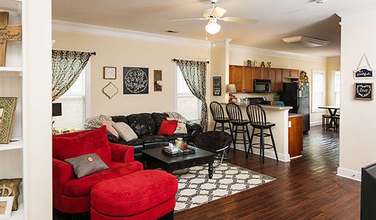 Living room and kitchen with bar and stools, dark sofa and bright red loveseat.