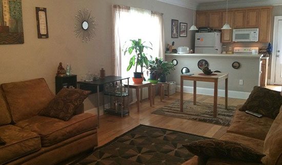Living room and kitchen with beige sofas, white appliances and snack bar.