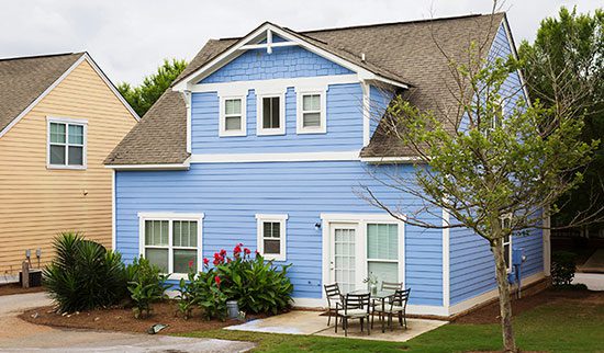 View of the back of a light blue two-story cottage with a patio